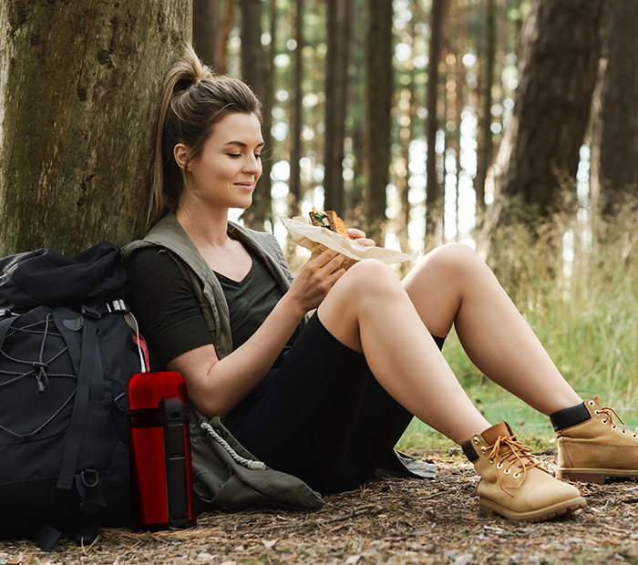 Woman on a hike, sitting under a tree, eating a sandwich